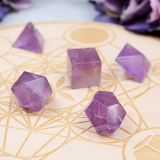 A collection of Amethyst crystal carvings arranged on a surface with a geometric pattern in the background.